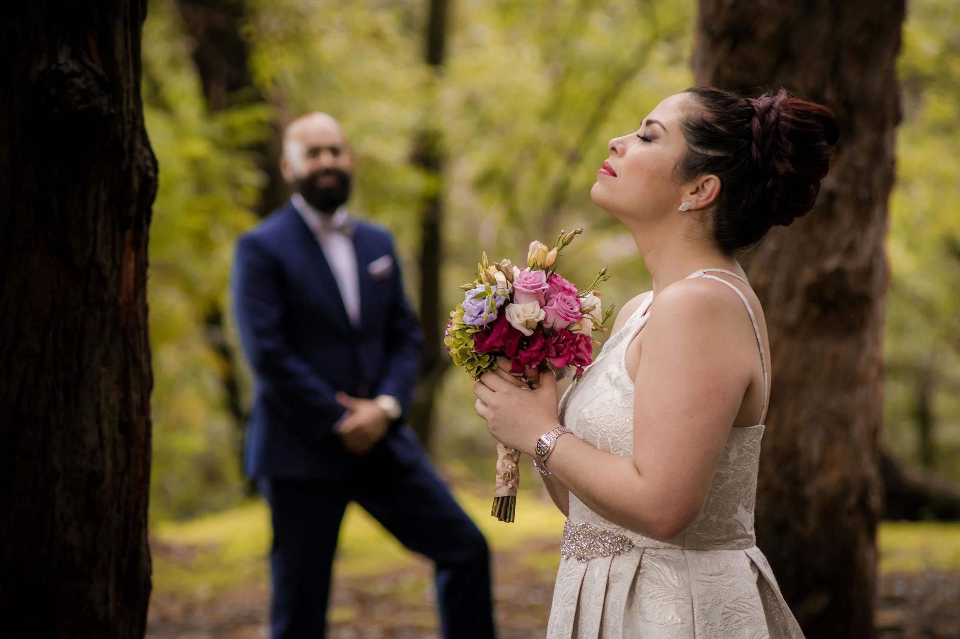 Panna młoda z bukietem w leśnej scenerii ślubu, pan młody w tle