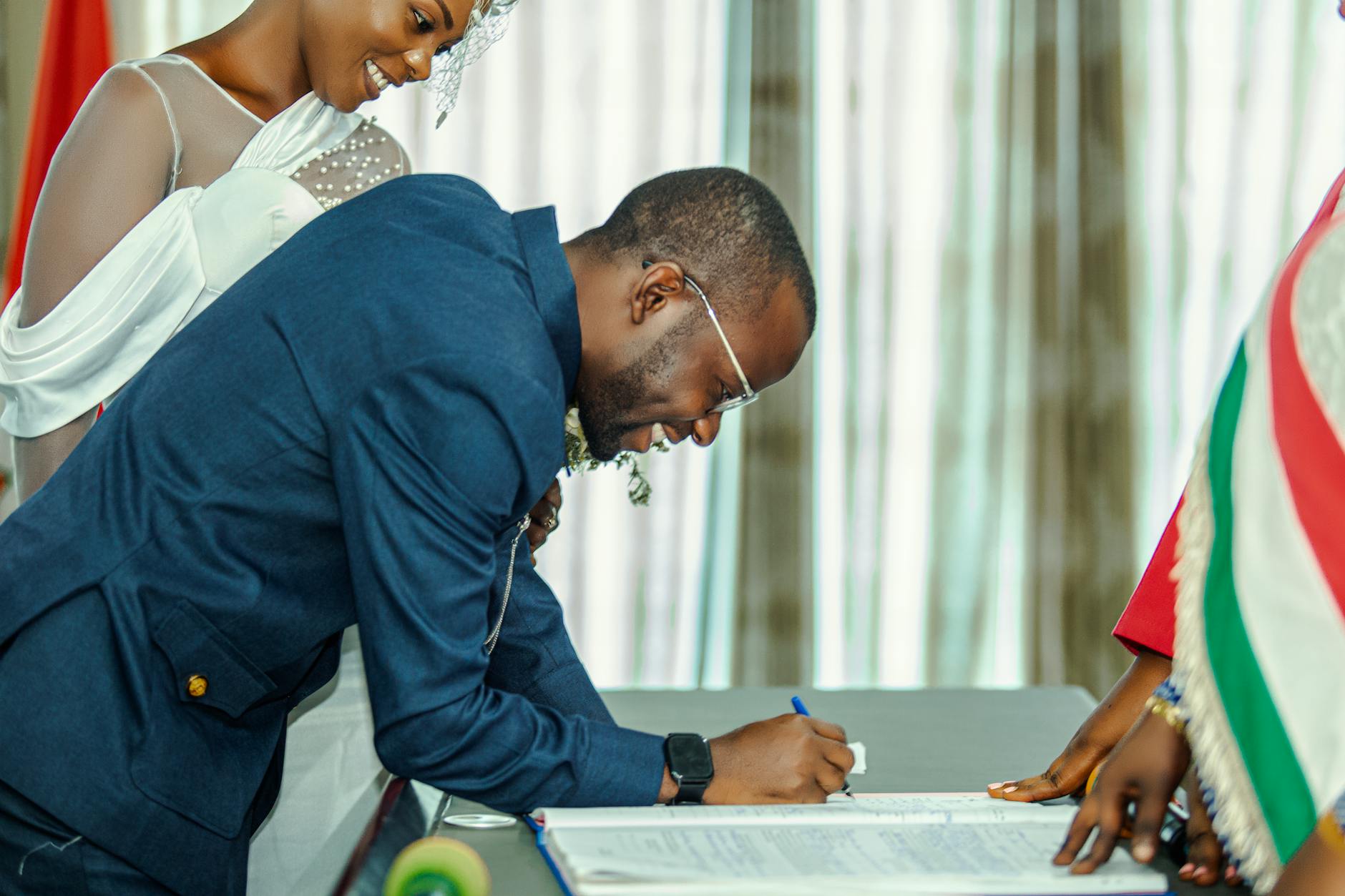 Pan młody podpisuje dokument ślubny, panna młoda patrzy z uśmiechem